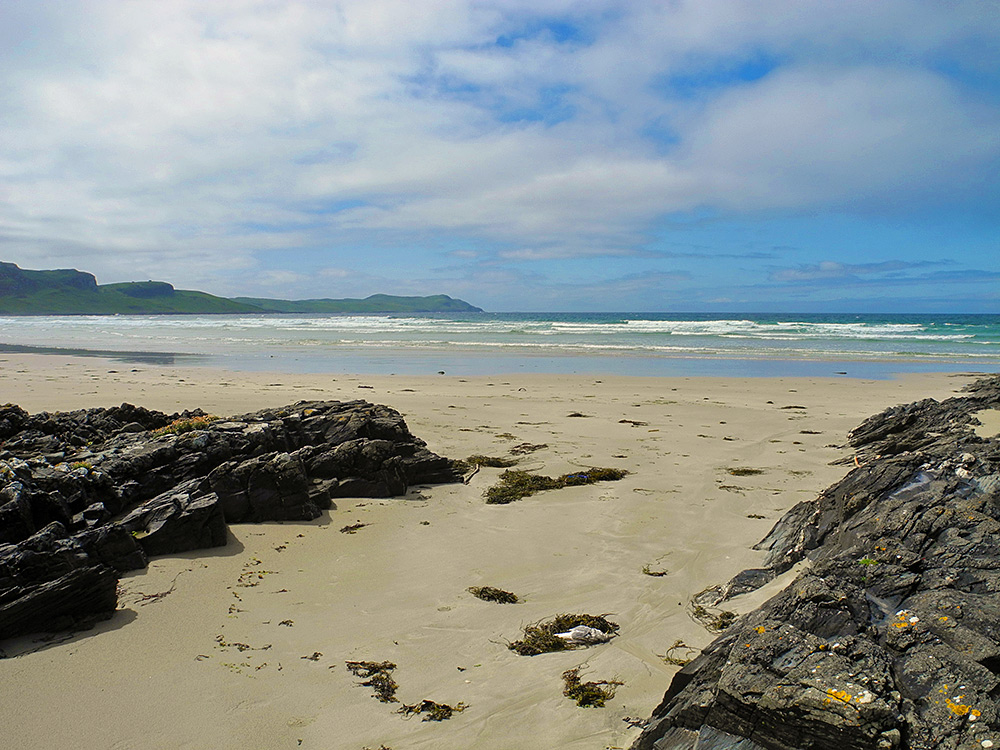 Picture of a view out between some low rocks over a sandy beach in a wide bay