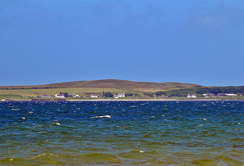 Picture of a small coastal settlement seen across a sea loch on a sunny afternoon