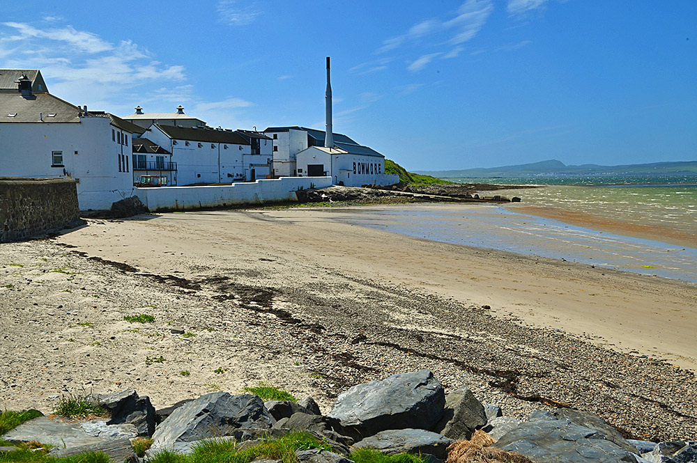 Picture of a small sandy beach at a sea loch, a whisky distillery (Bowmore) at the end of the beach