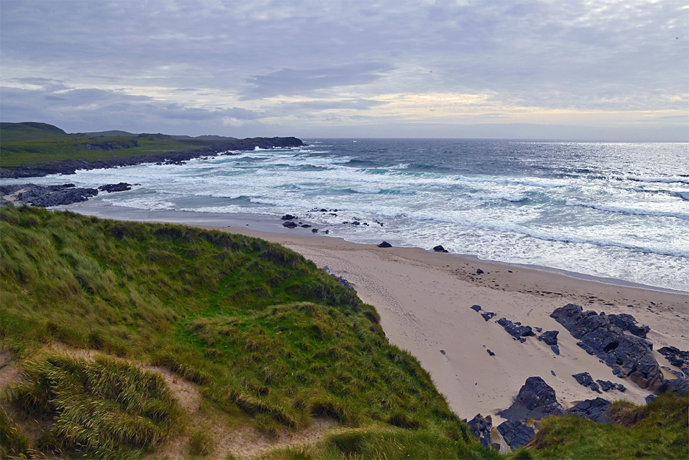 Picture of a view from a dune with sea grass over a sandy beach in a wide bay with breaking waves
