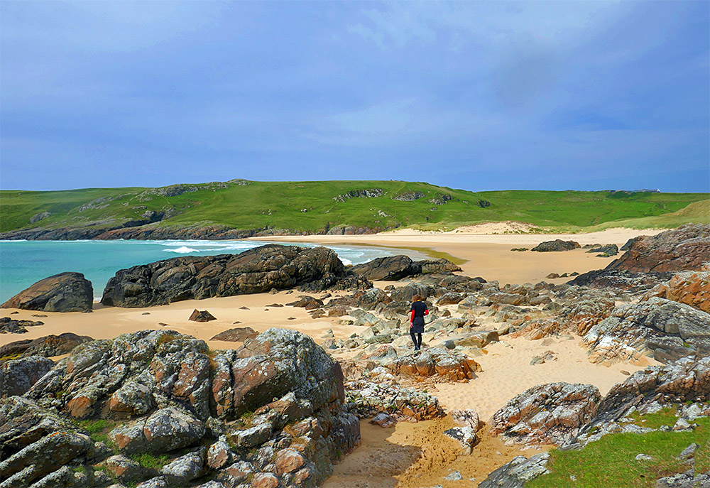 Picture of a person climbing over low rocks in a bay with a sandy beach