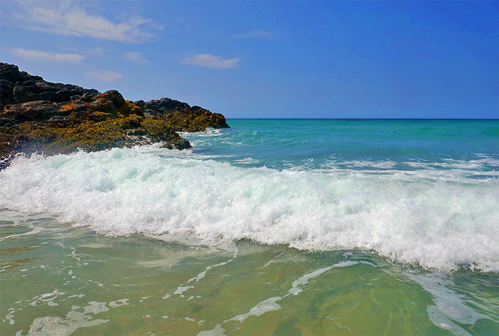 Picture of a breaking wave rolling out on to a beach near the end of the beach with rocky cliffs