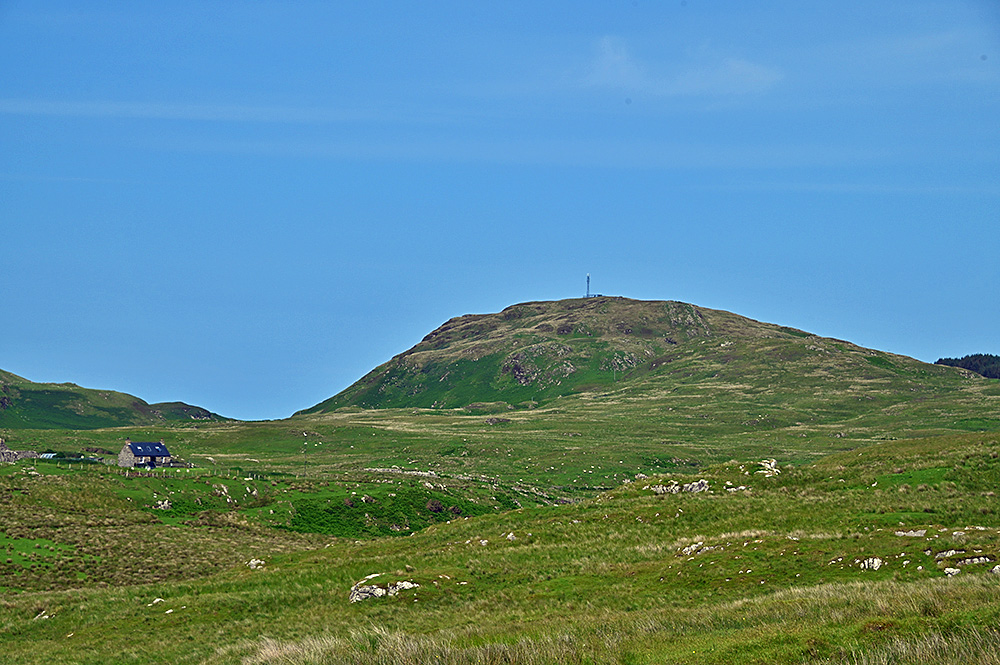 Picture of a lone rural house under a hill with a radio mast in a rugged landscape