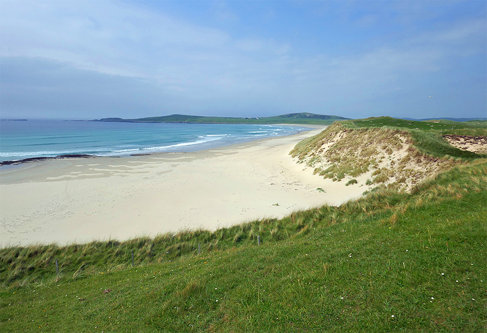 Picture of a sandy beach below sandy dunes with a grassy top in a wide bay