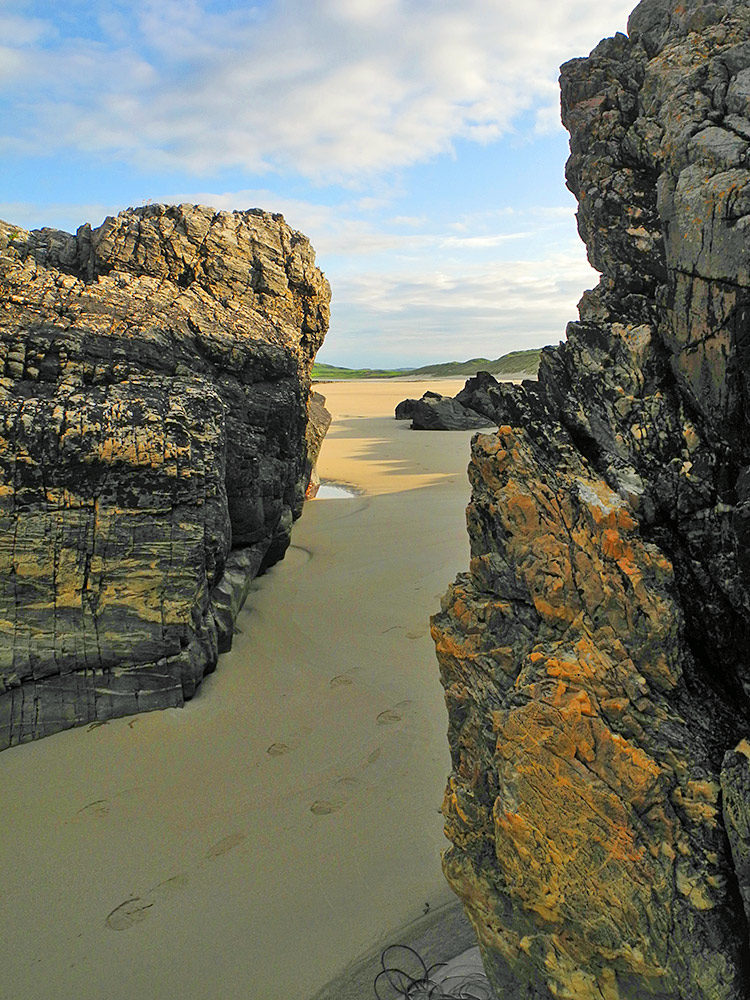 Picture of a sandy beach seen from a gap between rocks at the end of the beach