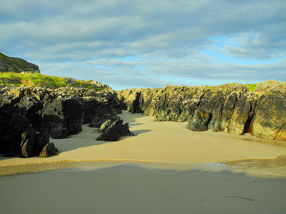 Picture of a gap in rocky cliffs forming a channel with a sandy beach bottom in some beautiful June morning sunshine