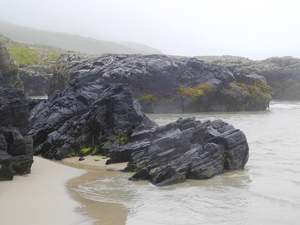 Picture of some large rocks and cliffs at the end of a sandy beach on a damp morning
